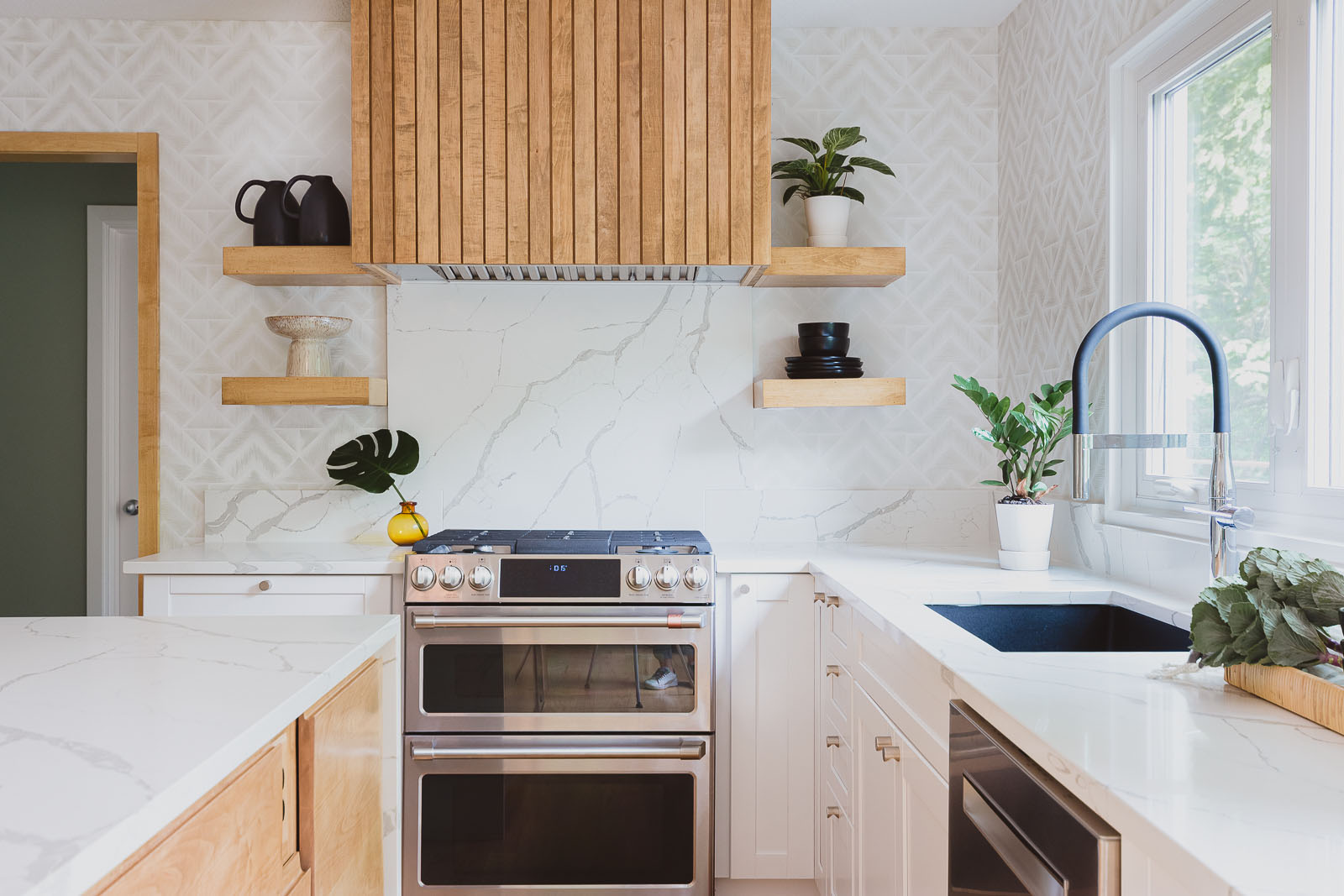 This custom renovated kitchen is featured on the Interior Design for Homeowners page for Sara Svehla Interior Design's website. The image showcases a gorgeous bubble chandelier over a marble-esque waterfall island. The kitchen has lots of custom wood slats and a white herringbone tile on the walls.
