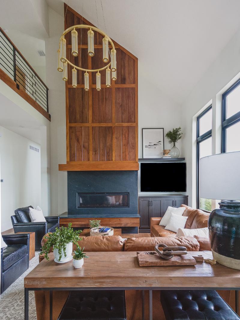 The leather sectional is in front of the titanium suede granite fireplace with a custom wood mantle and brass chandelier. Adjacent are two black leather accent chairs in the Haven custom home project.