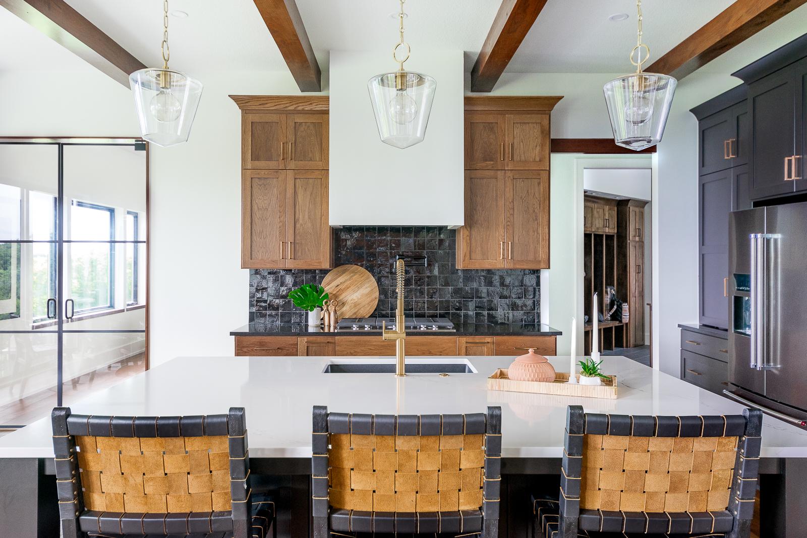 Custom-designed kitchen with white countertop island, black woven barstools, black tiled backsplash, and custom cabinetry at the Haven custom home project.