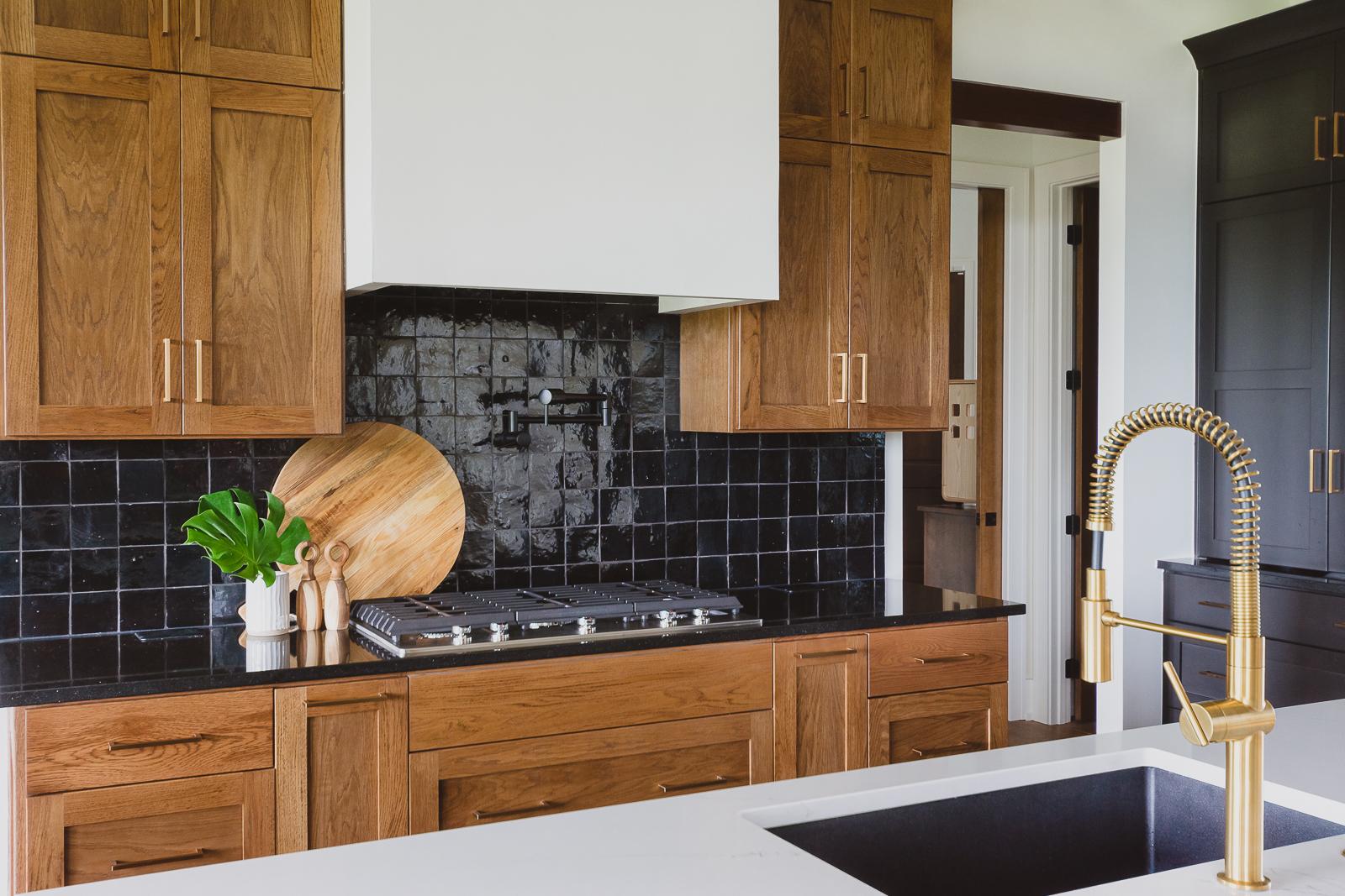Kitchen shot featuring stove and vent hood with black tiled backsplash and negresco countertops. 