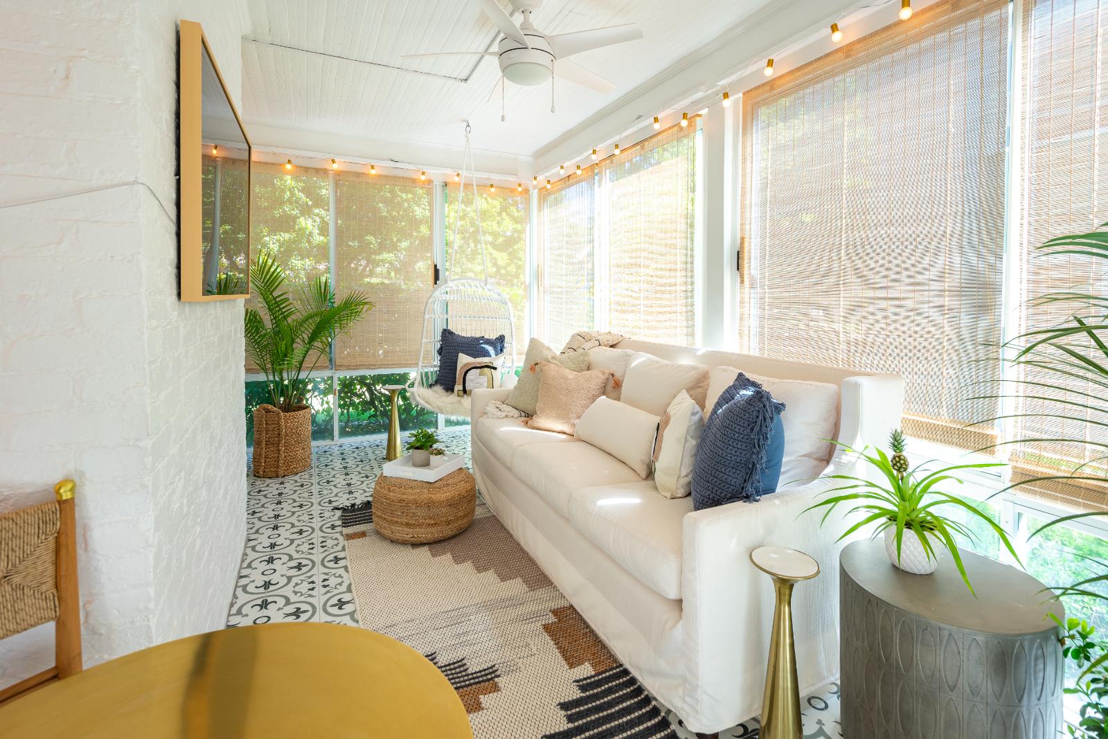 Historic home renovation featuring a sunroom with a cream colored sofa, hanging accent chair in one corner, and various indoor plants. 