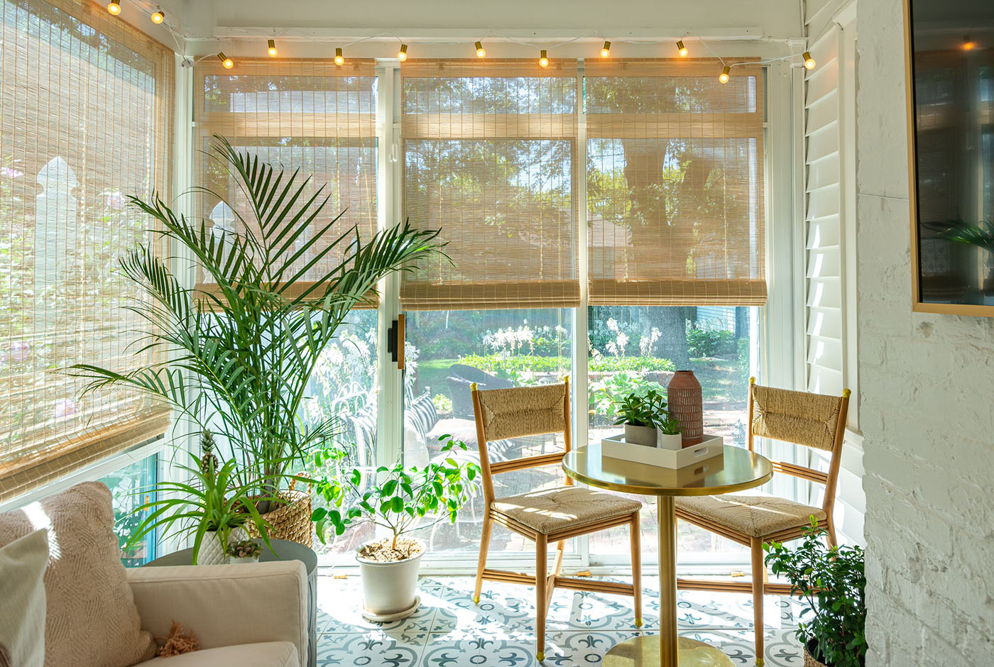 historic home renovation showcasing a small seating area in the sunroom. The space has a small dining table and two accent chairs with custom rattan roller shades covering the windows.
