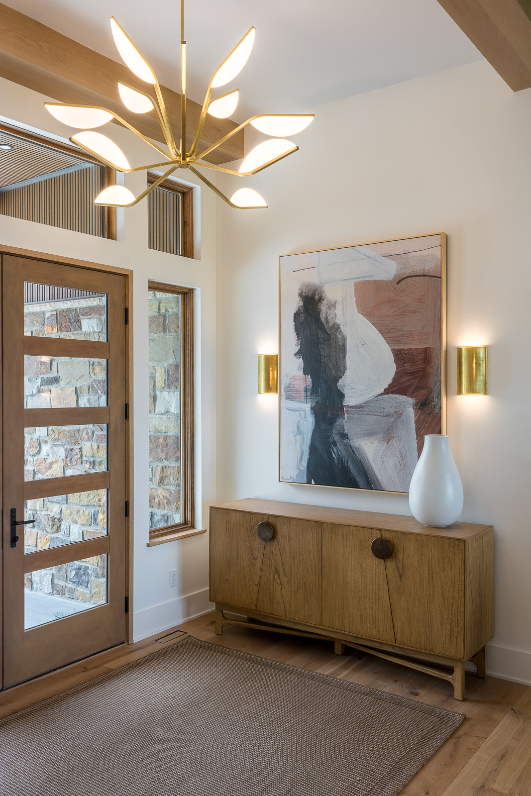 Featured on the interior design for homeowners page of Sara Svehla Interior Design's website, this Artisan Home in Holt, Missouri, entryway with specialty lighting, chandelier, and lighting framing a large abstract painting.