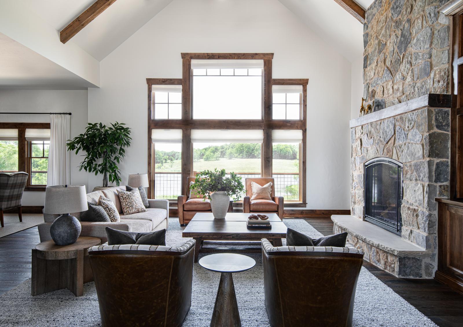 Artisan Home - Refined rustic family room overlooking a large pond. Featuring trusselwood beams on the ceiling, and a natural stone fireplace with custom leather chairs, plush seating and a large coffee table. 