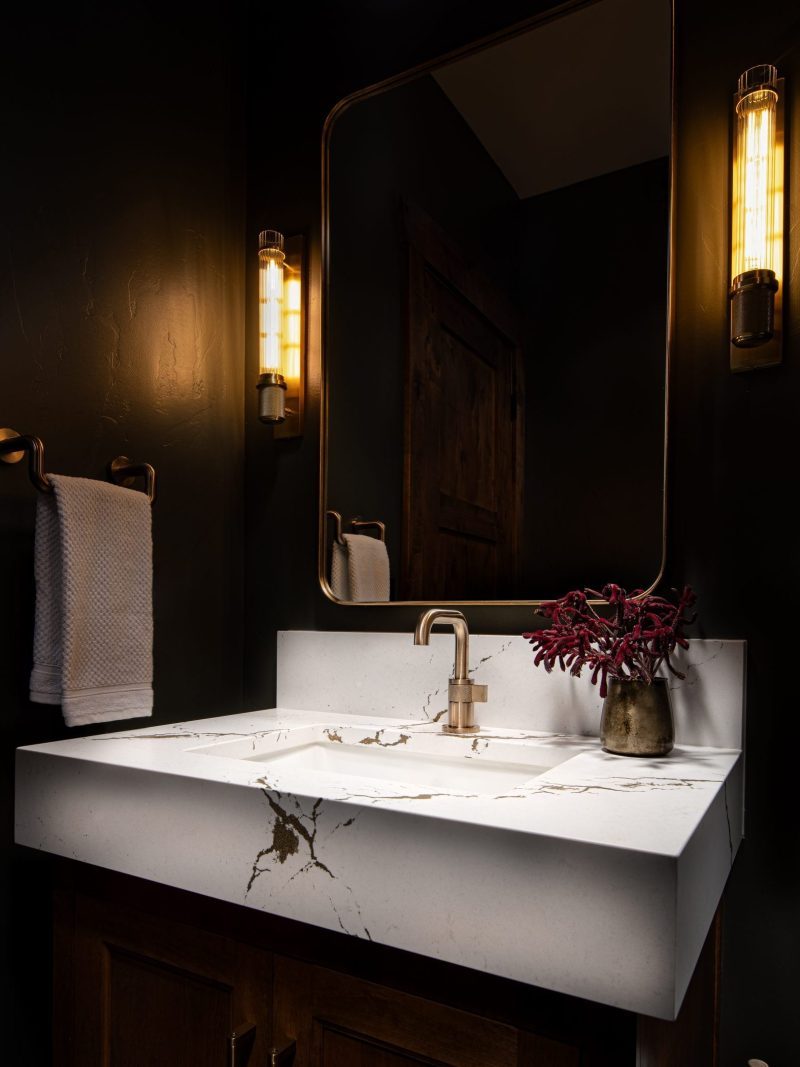 Dark and moody guest bathroom shot of white countertop with brass hardware.