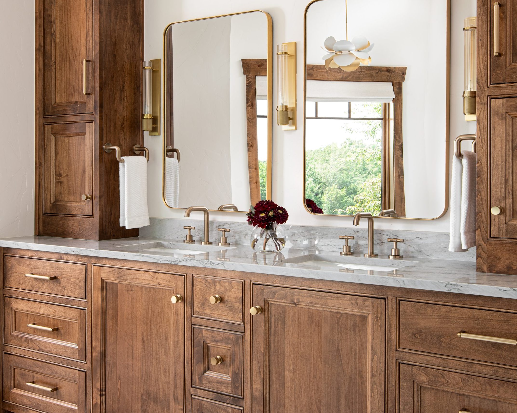 Primary bathroom with double vanity featuring custom wood cabinetry, quartzite countertops and brass hardware.